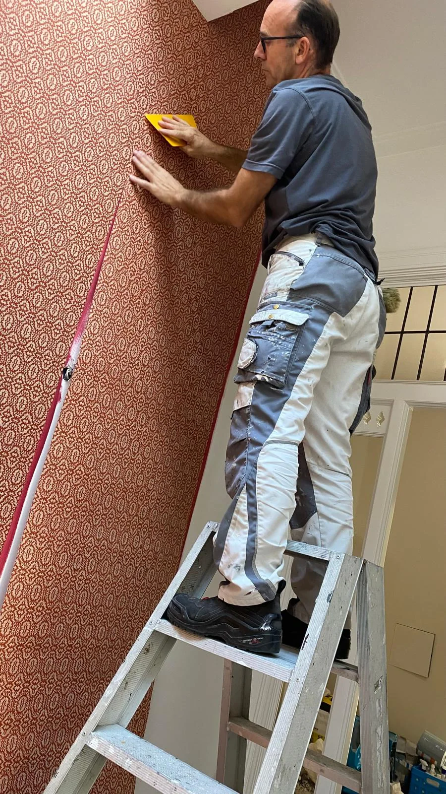Schilder en behanger tijdens het zorgvuldig aanbrengen van patroonbehang, gezicht en werk in beeld