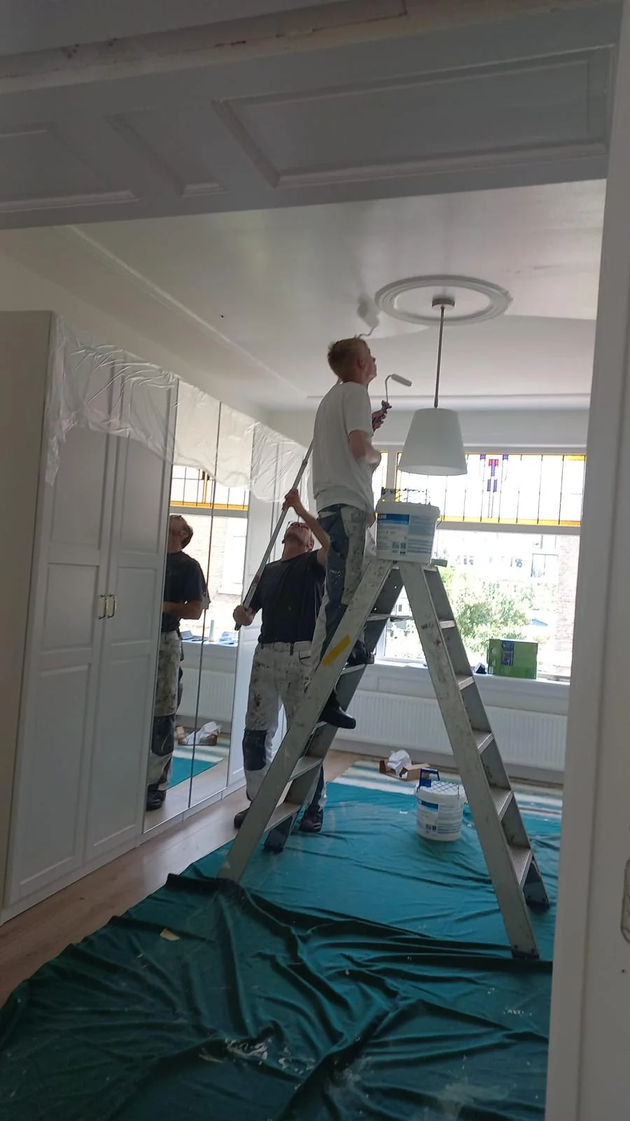 Schilderwerk aan een hoog plafond in een karaktervolle kamer.